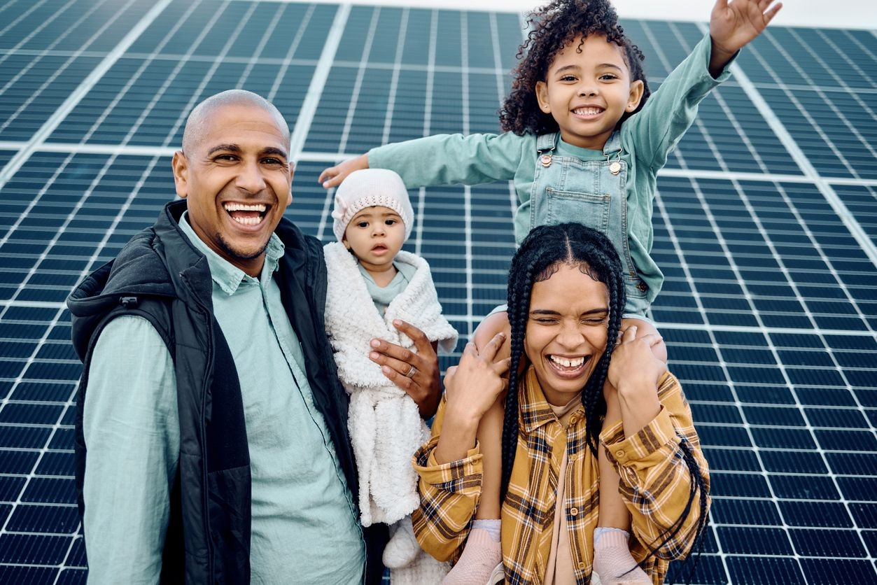 Happy family posing in front of solar panels under a clear sky.